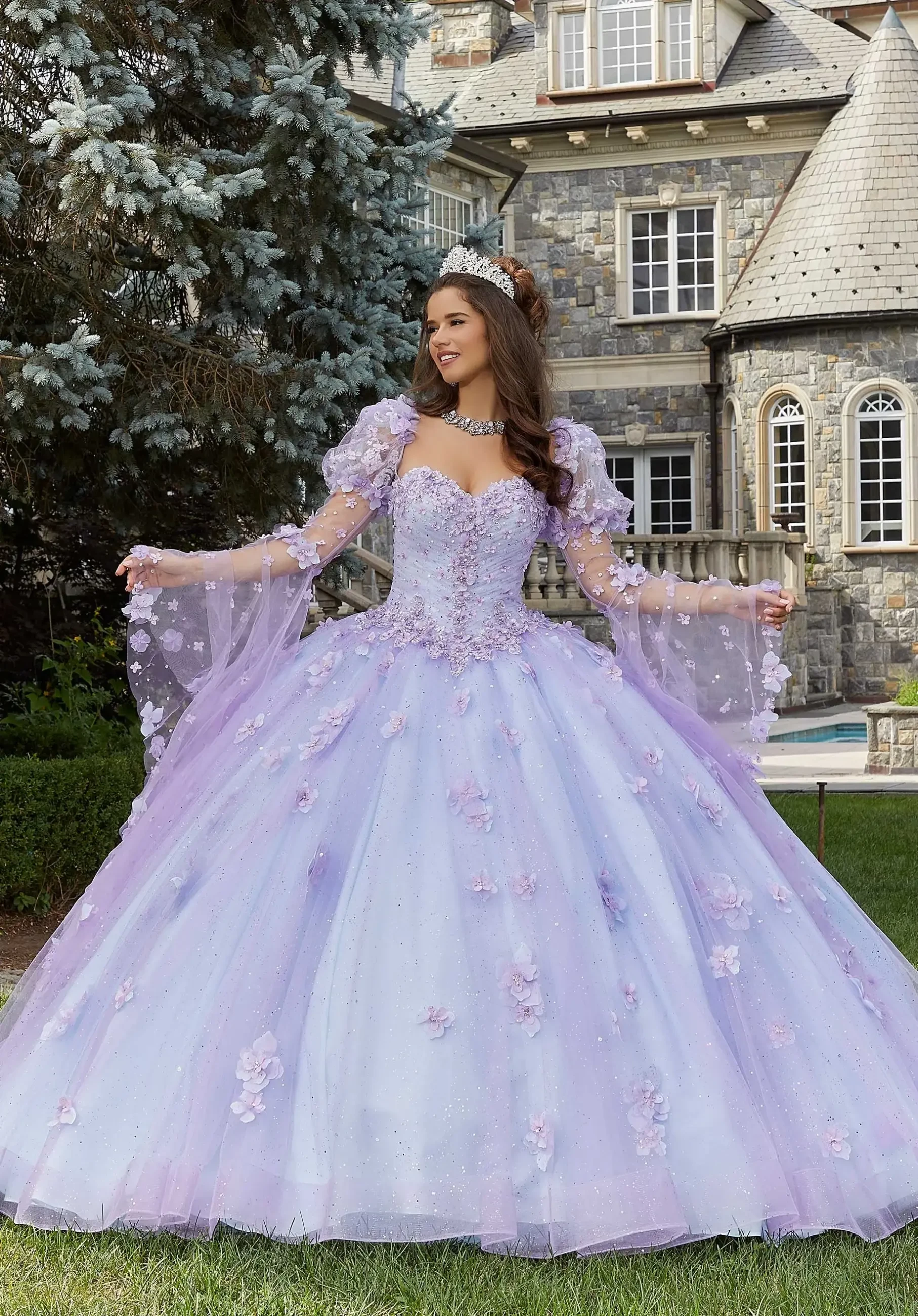 A person wearing a lavender ball gown with floral embellishments, standing in a garden with a stone mansion in the background.