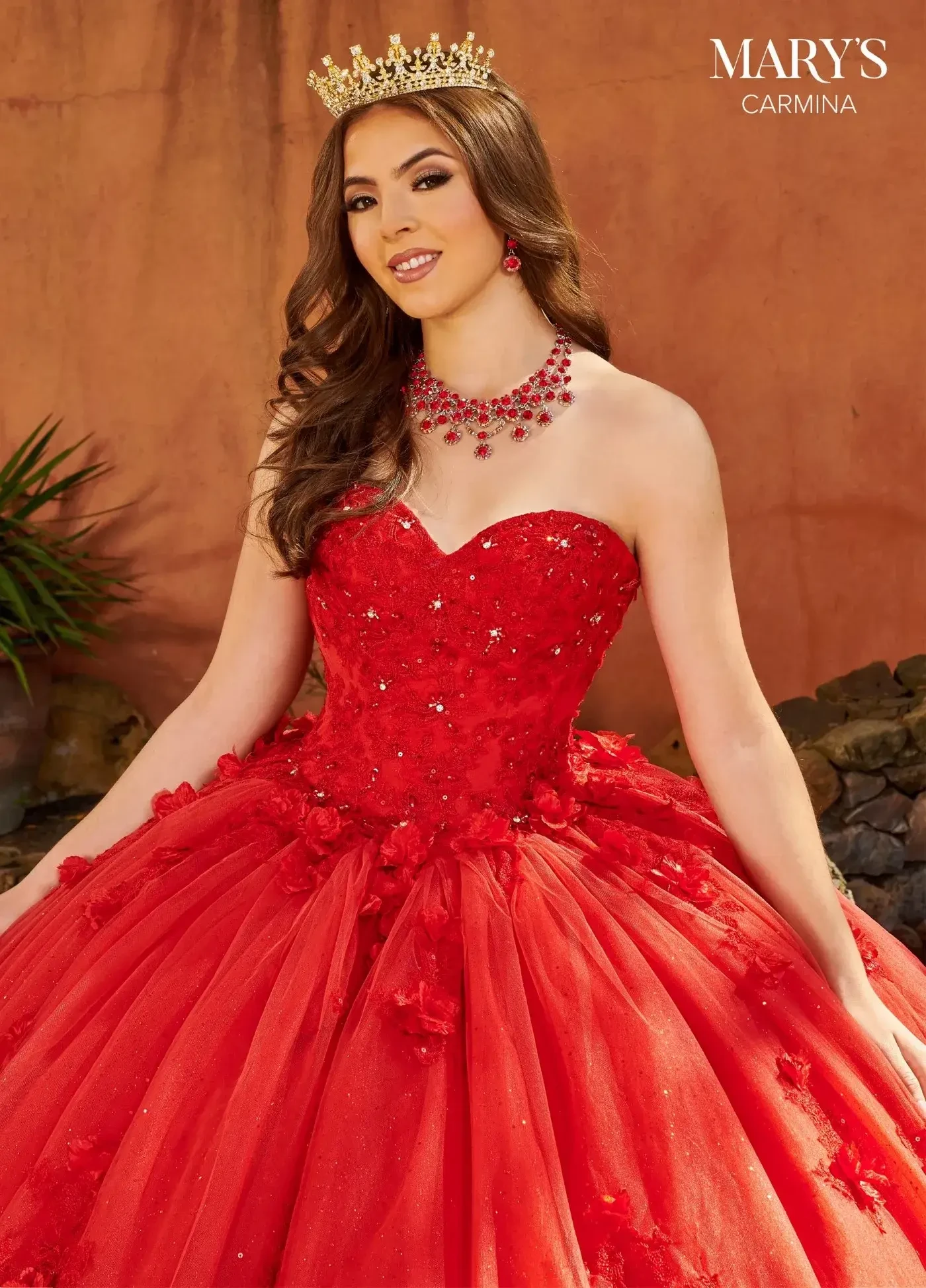 A young woman in a strapless, red ball gown adorned with sequins and floral details, wearing matching jewelry and a tiara.