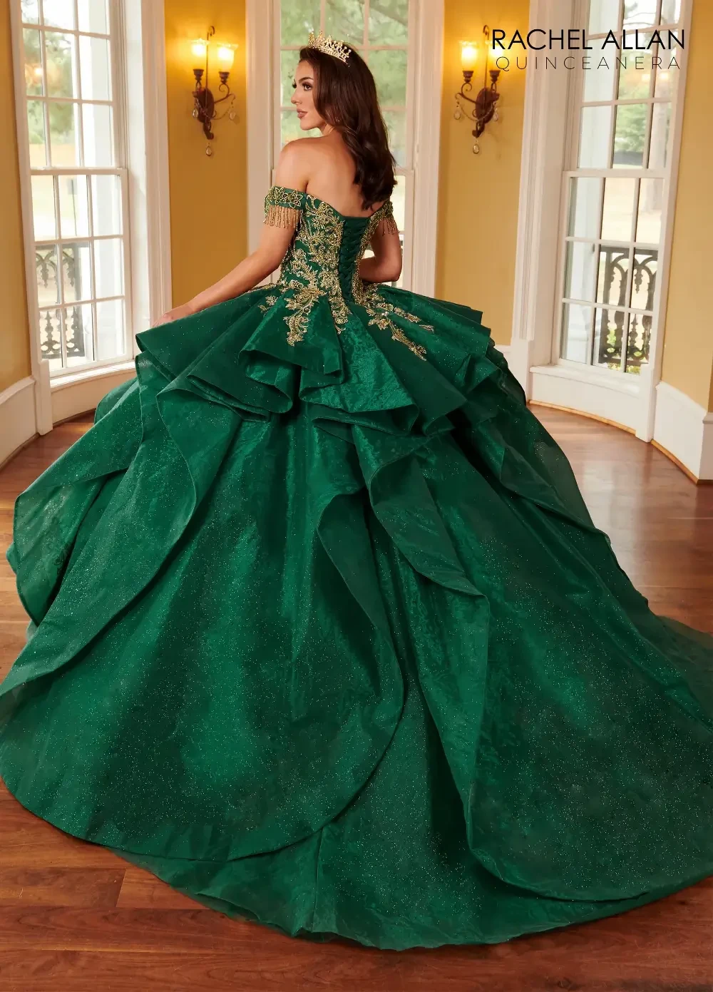 A young woman wearing a detailed green ball gown with off-the-shoulder sleeves and layered ruffles, standing in an outdoor setting.