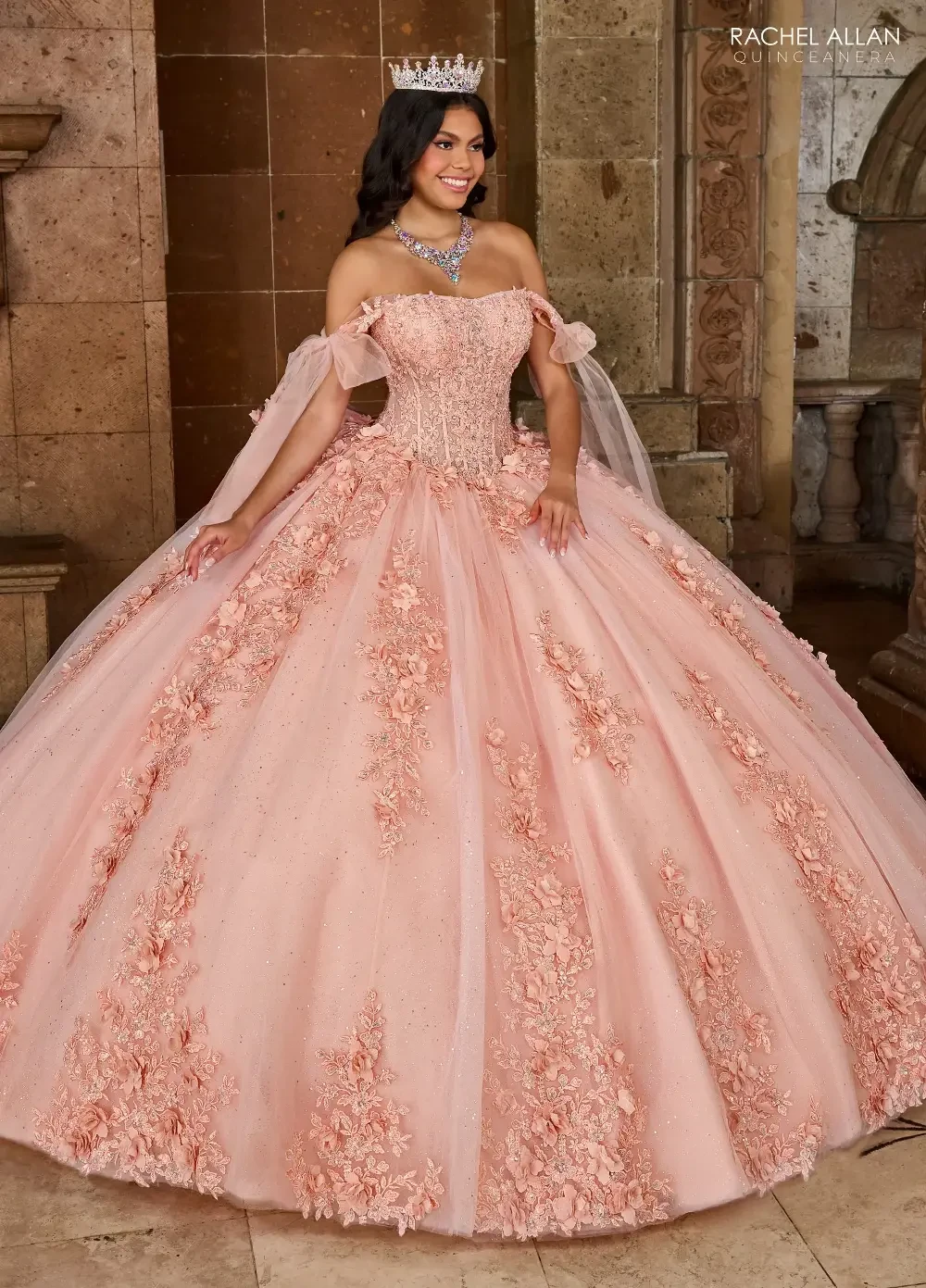 A woman in a large, elegant pink ball gown adorned with floral details, wearing a crown and standing in a grand, ornate setting.